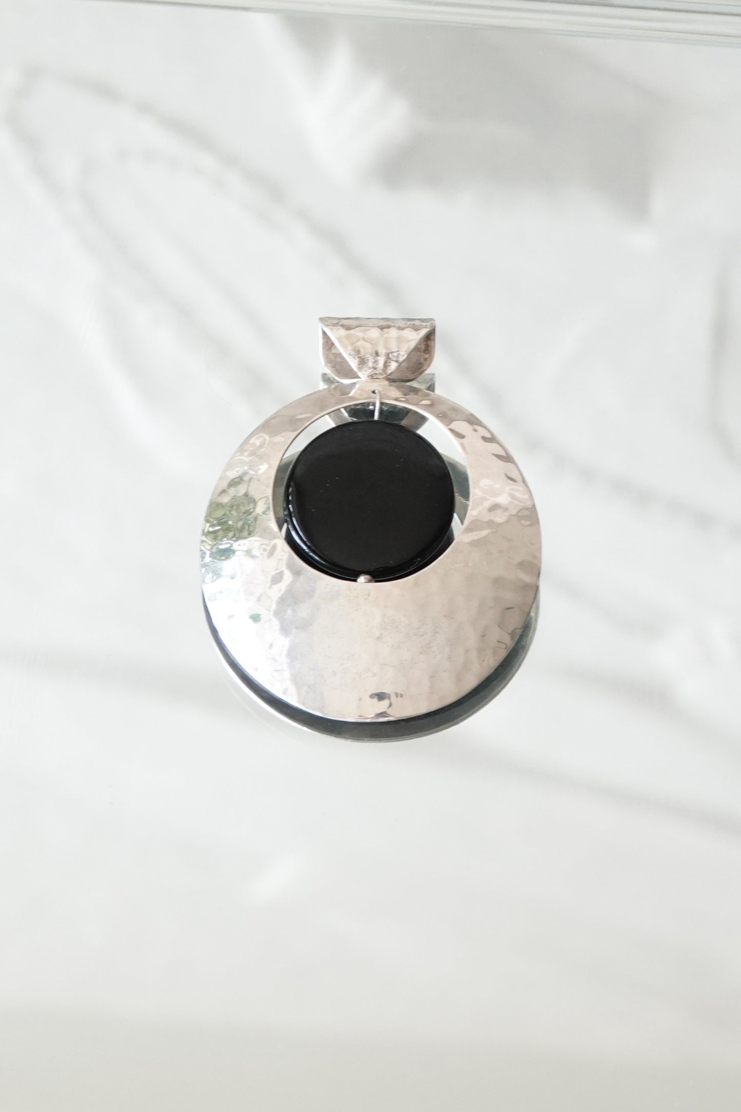 Hammered sterling silver disc pendant with black onyx cabochon, styled on glass