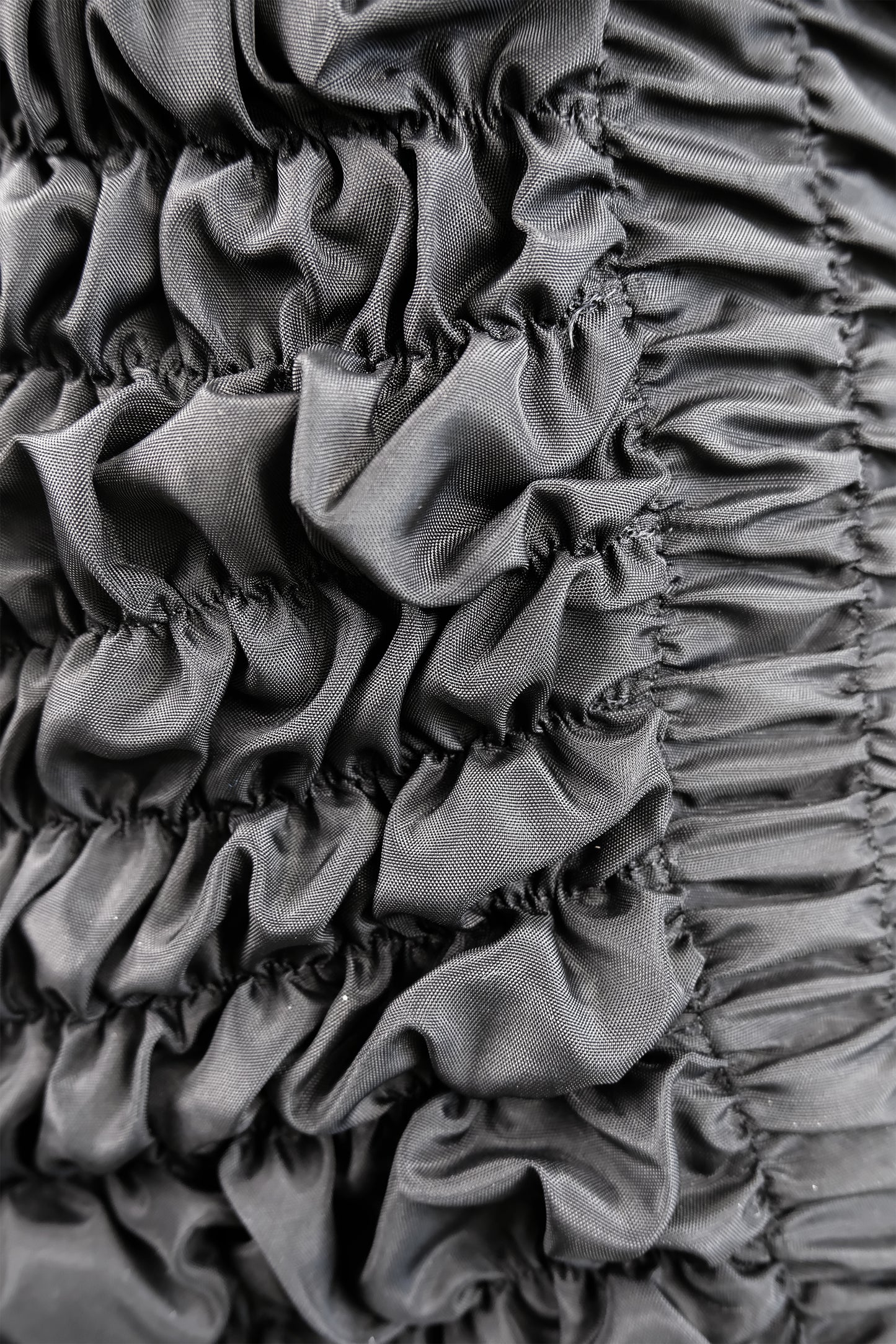 Comme des Garçons 1989 black smocked bib dress fabric detail: close-up macro of intricate smocking technique showing gathered rows of black fabric creating voluminous three-dimensional tactile texture, circa 1989