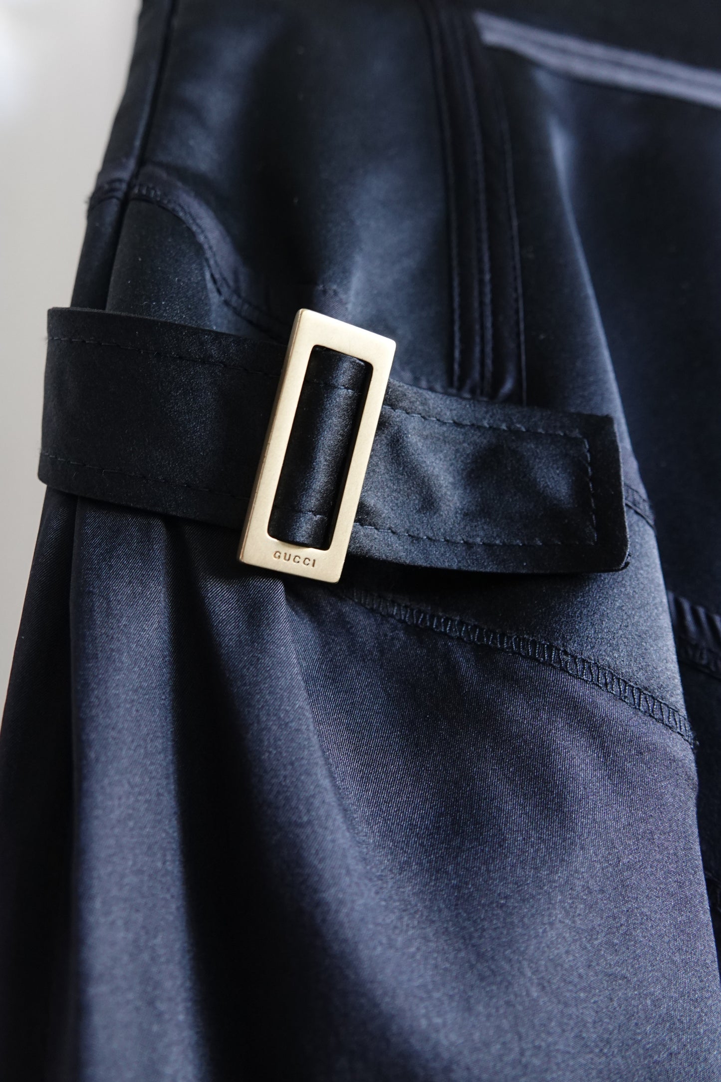 Tom Ford for Gucci FW03 black silk skirt hardware close-up: gold-tone rectangular buckle with engraved "gucci" logo on black silk strap, authentication detail, Fall 2003