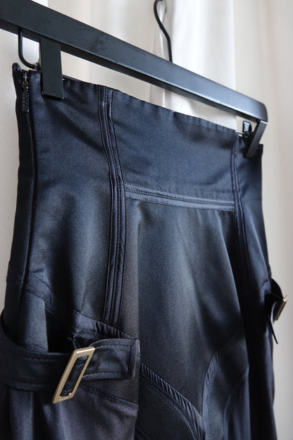 Tom Ford for Gucci FW03 black silk corset skirt on hanger: three-quarter back view showing back zipper, structured high waist, bias-cut flared hem and side strap with gold-tone buckle, Fall 2003