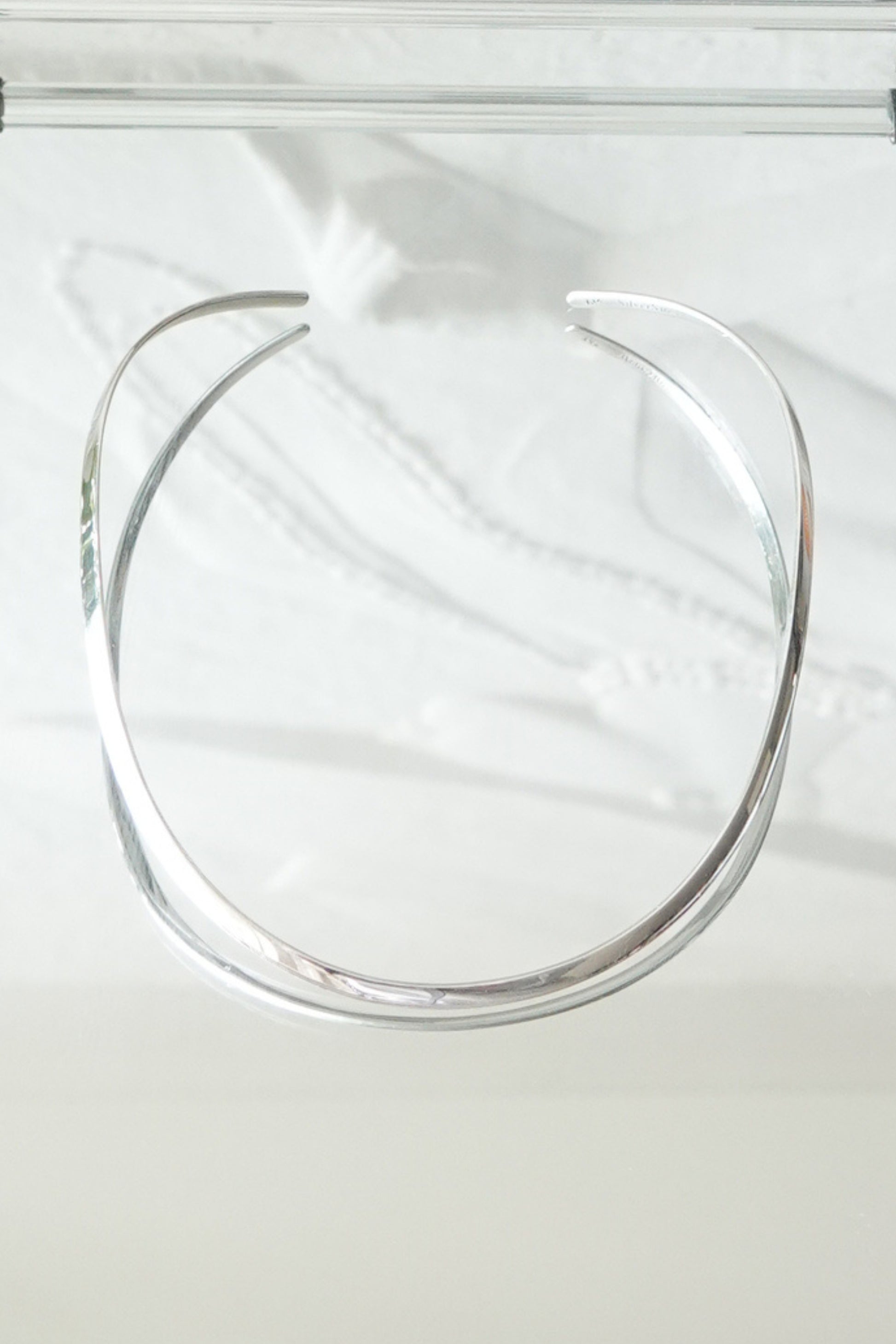 SilverSue sterling silver neck cuff styled on glass surface