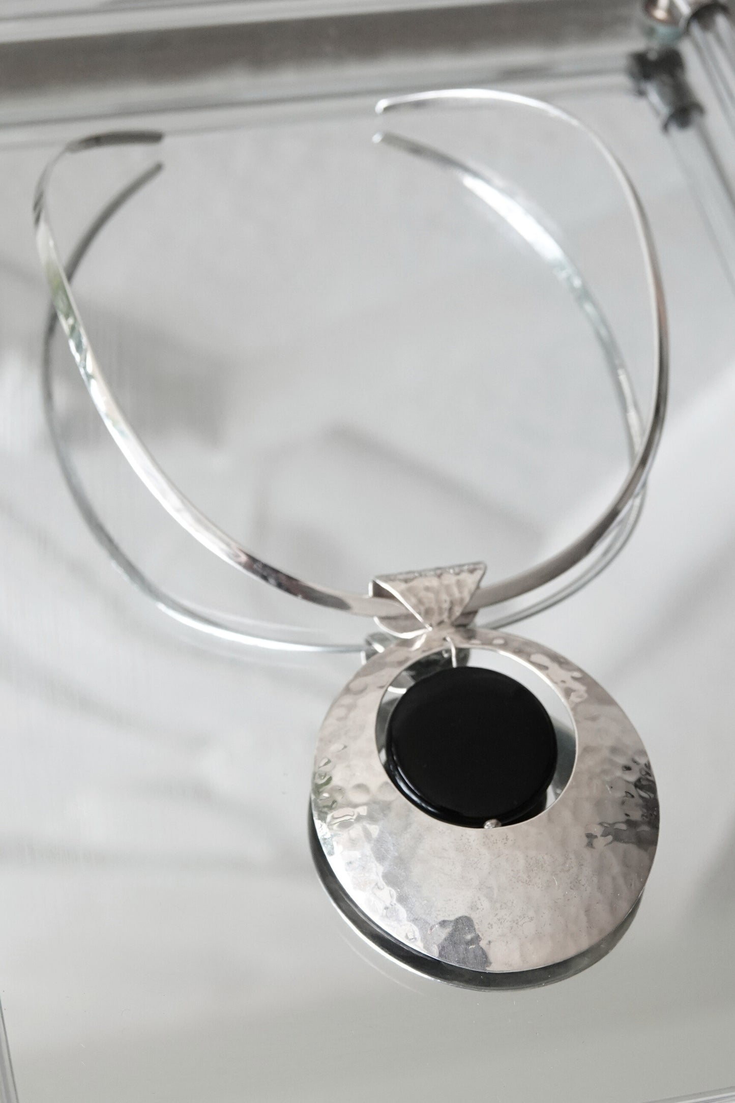 SilverSue neck cuff and pendant styled on glass, overhead angle