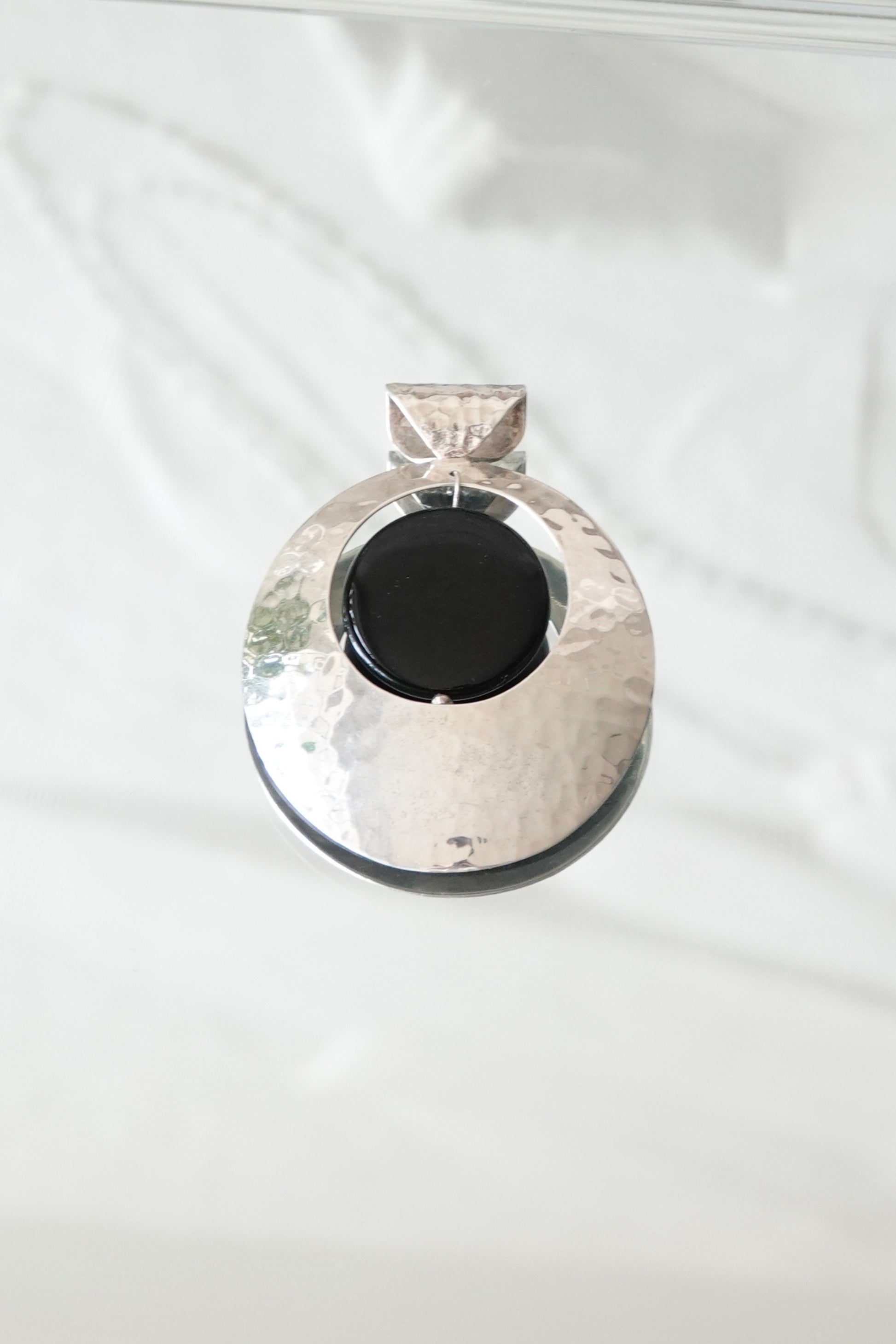 Hammered sterling silver disc pendant with black onyx cabochon, styled on glass