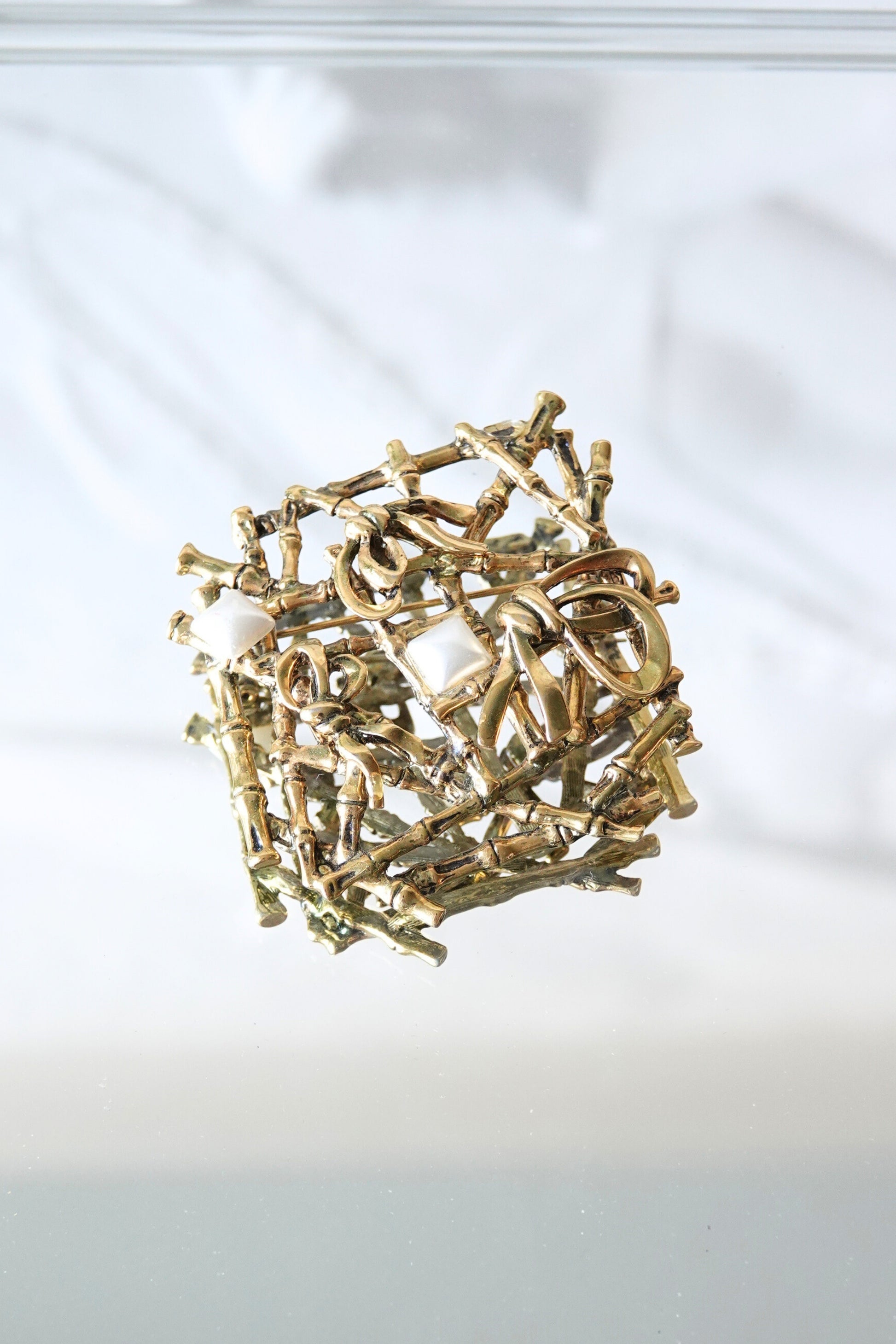 Gold-tone bamboo lattice brooch — front on glass surface