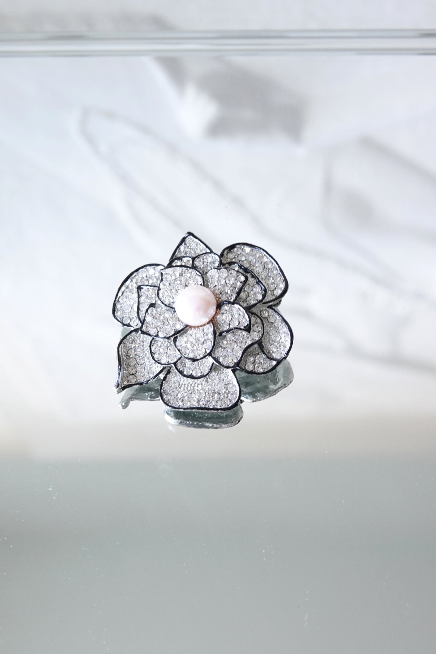 Vintage rhinestone camellia brooch, faux pearl center — styled top view on reflective surface — Disco Palma