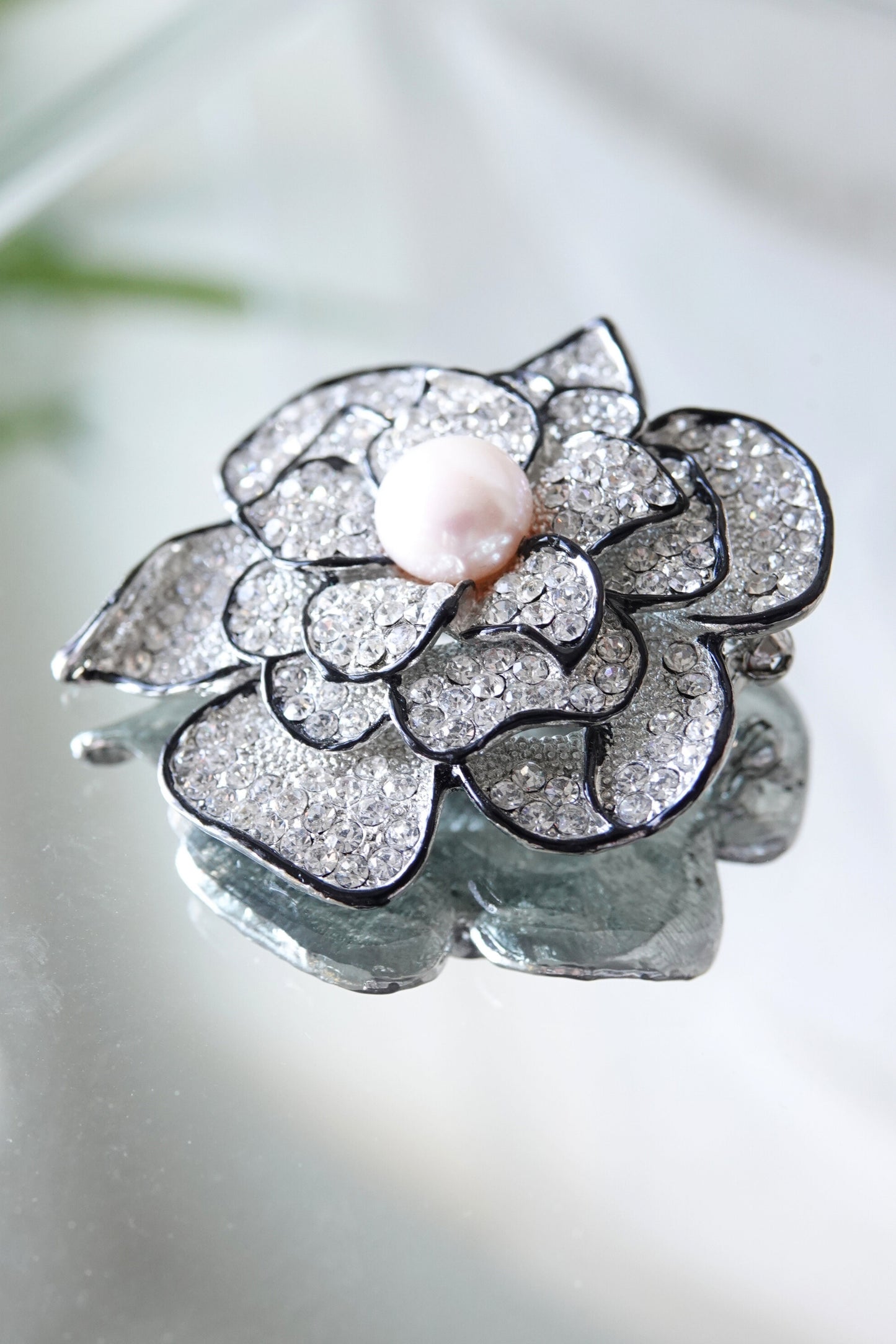 Vintage rhinestone camellia brooch, petal detail — styled angled view on reflective surface — Disco Palma