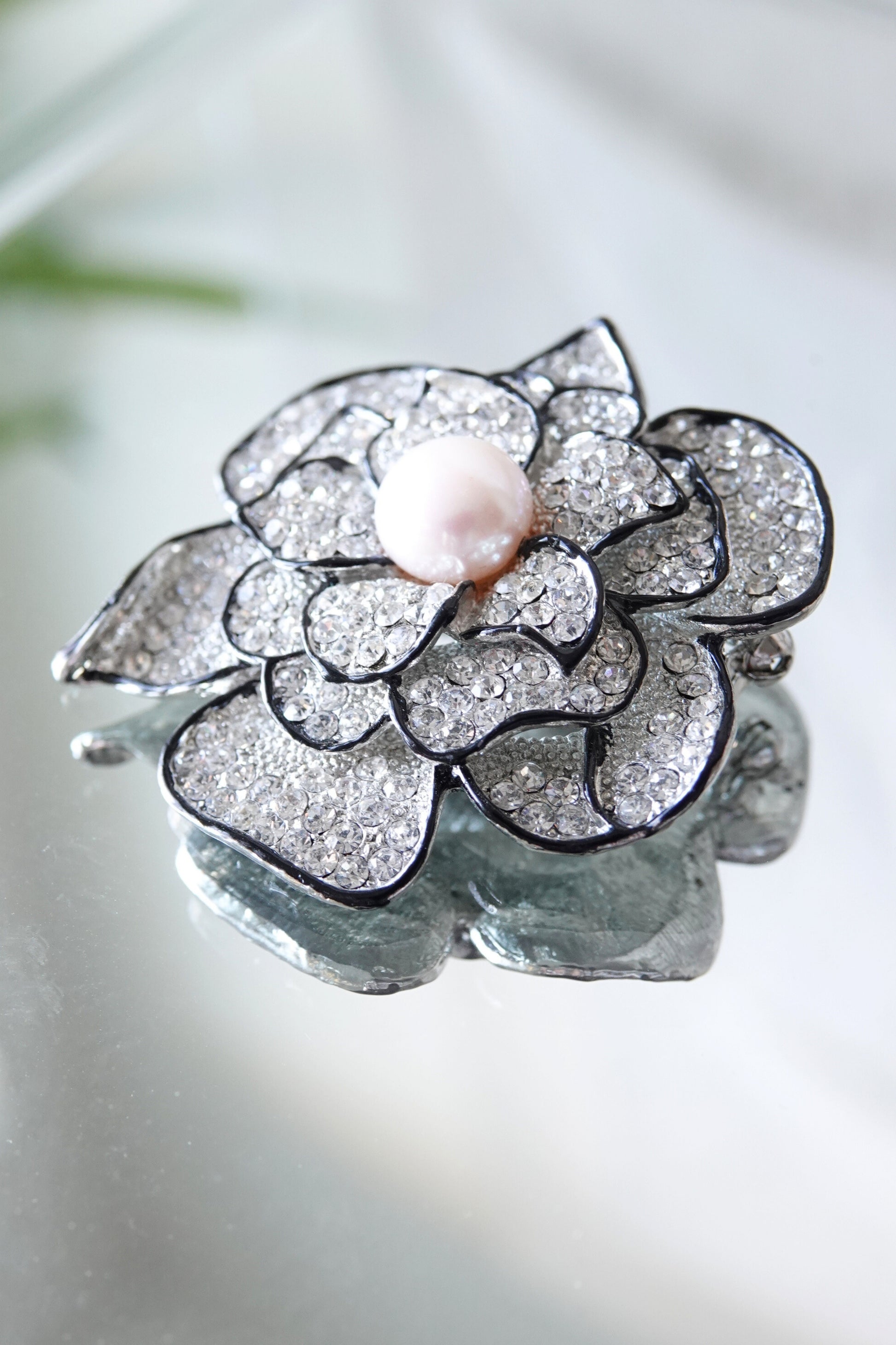 Vintage rhinestone camellia brooch, petal detail — styled angled view on reflective surface — Disco Palma