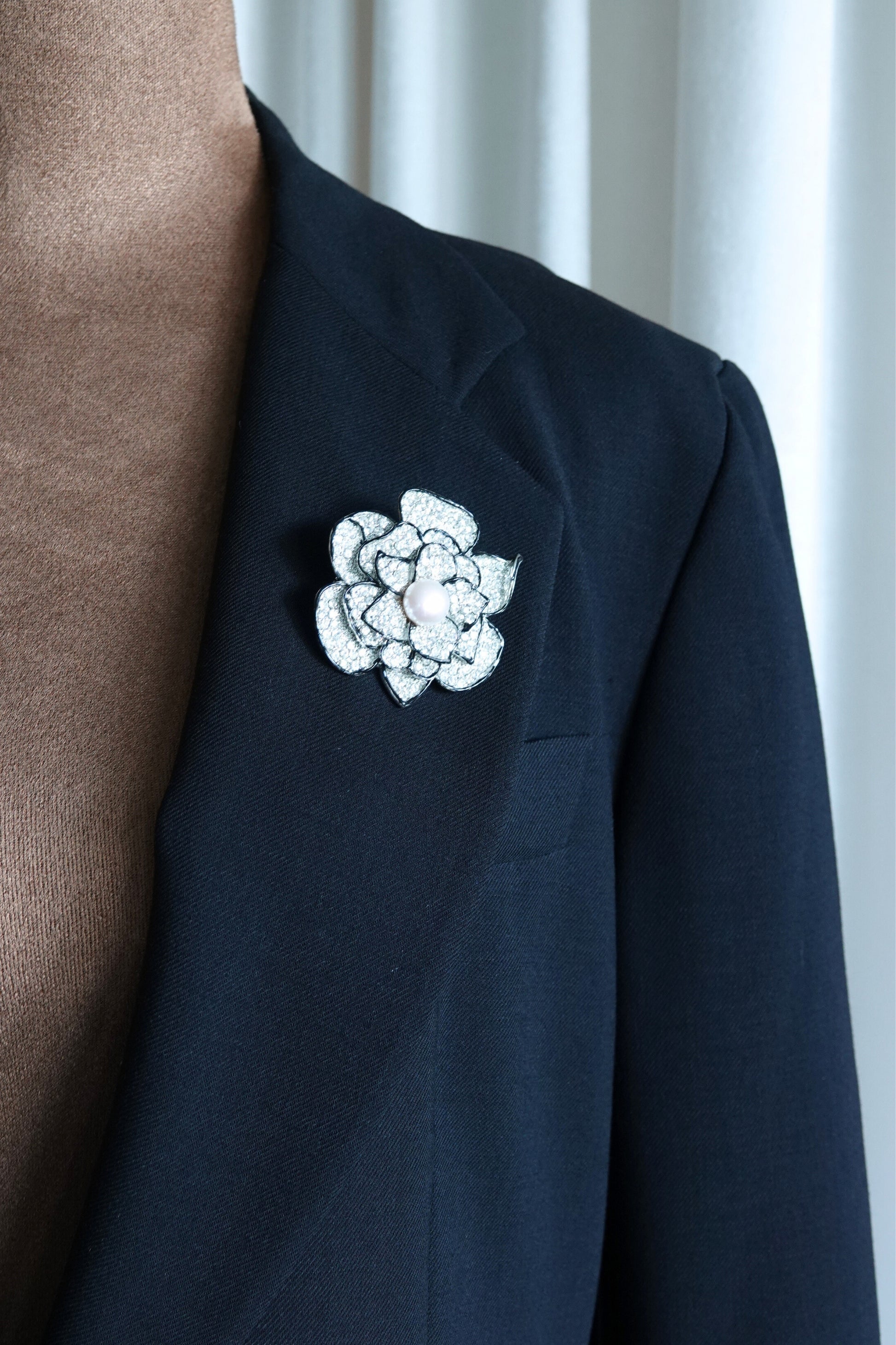 Rhinestone camellia brooch — three-quarter view on glass surface
