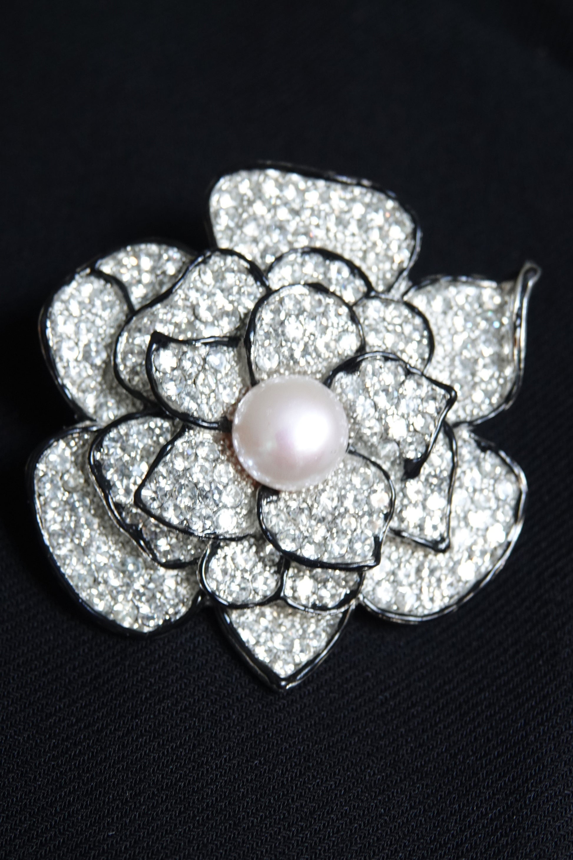 Pavé rhinestone flower brooch with pearl center — styled on dark background