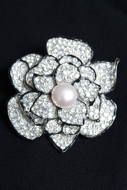 Pavé rhinestone flower brooch with pearl center — styled on dark background