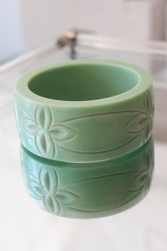 Carved celadon Bakelite bangle — styled on glass surface