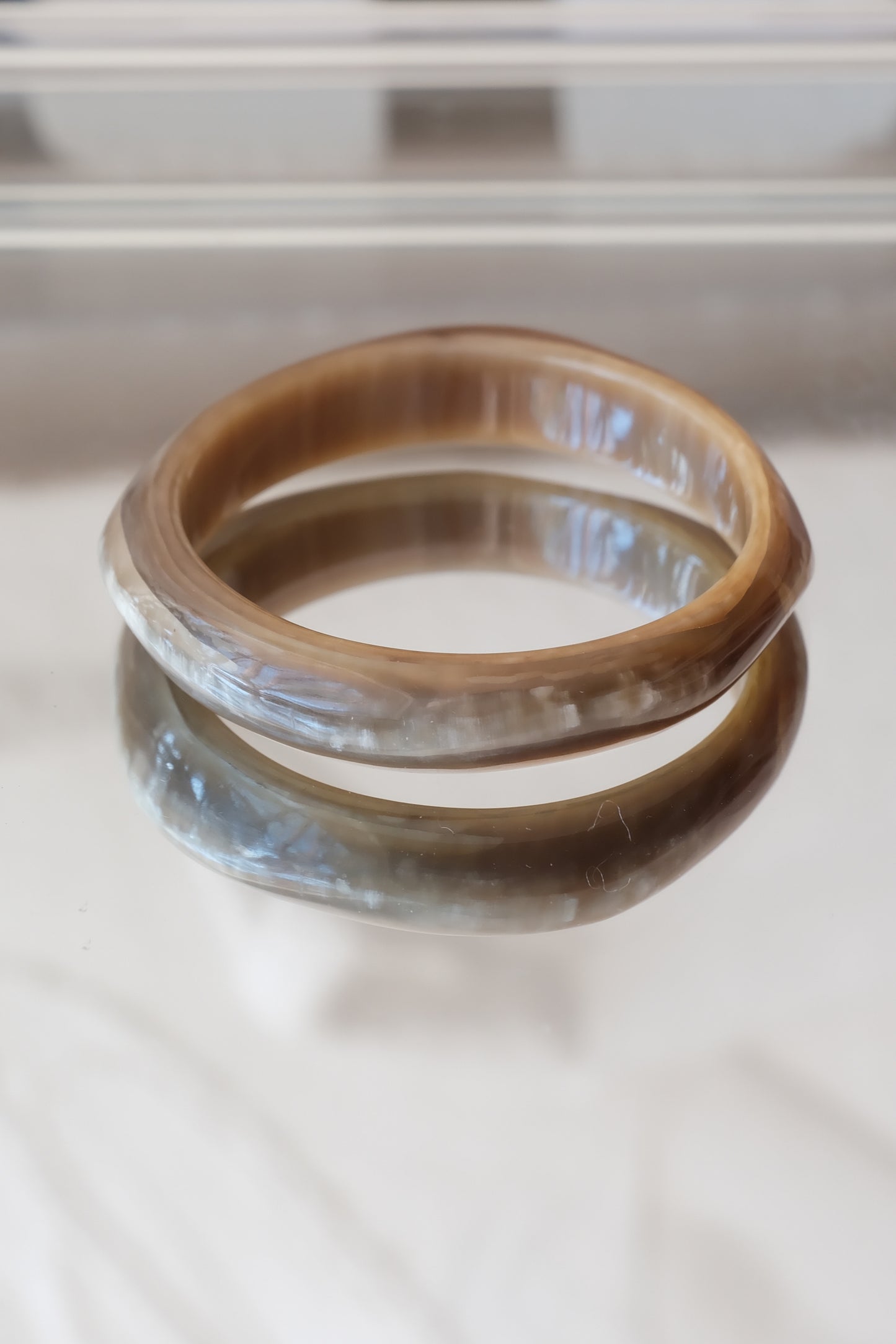 Natural horn bangle — styled upright on reflective white surface, natural light