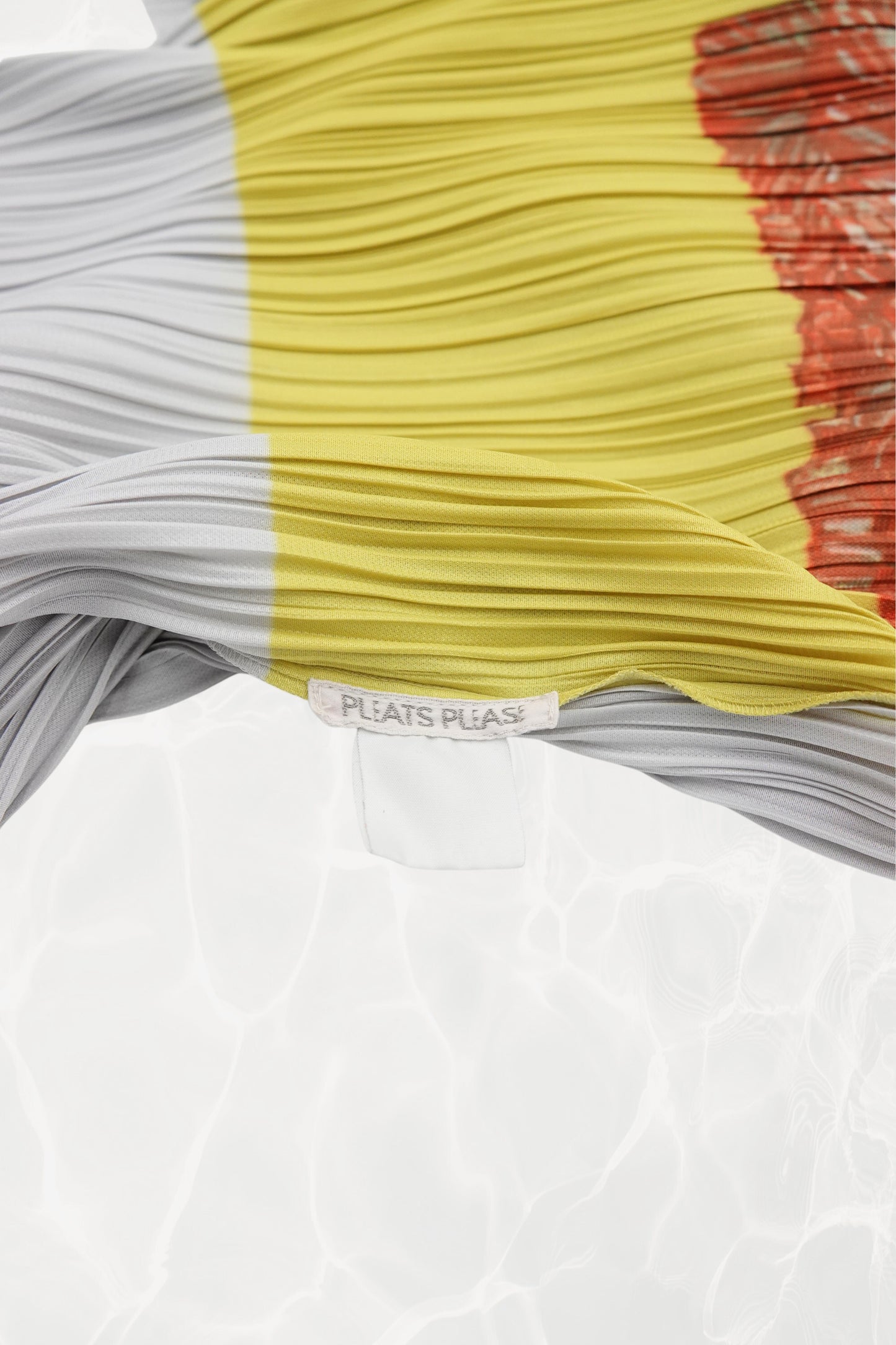 Pleats Please Issey Miyake x Mimi Yokoo carnation dress label detail: interior PLEATS PLEASE brand label at waist seam  with white and yellow pleated panels and carnation print, c. 2000