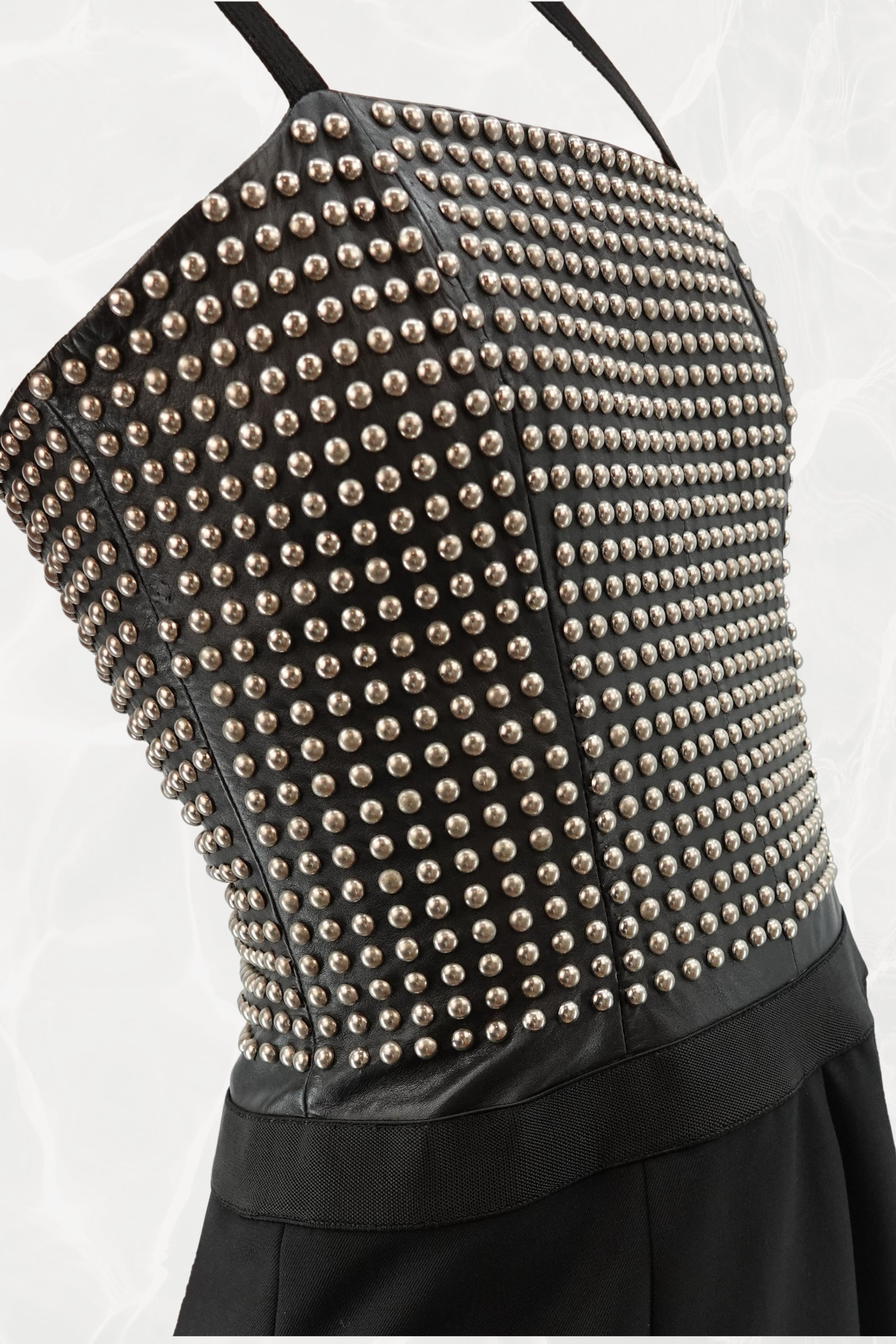 Loewe by Narciso Rodriguez AW01 studded leather dress three-quarter view: angled front showing fitted metal-studded leather corset bodice with elastic shoulder straps and paneled black silk flare skirt, AW2001
