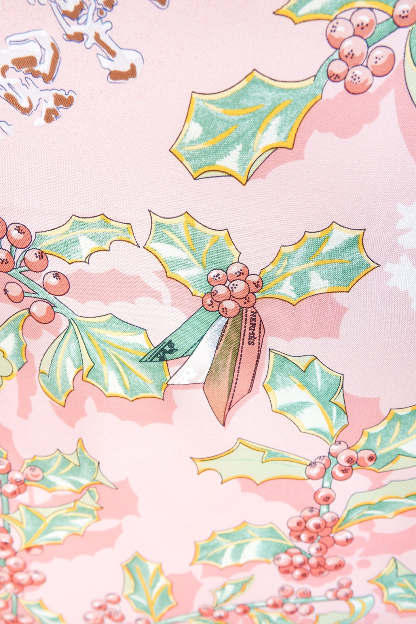 Hermès Neige d'Antan Carré 90 close-up: HERMÈS ribbon tied on illustrated holly and berry sprig, botanical winter motif on pink silk twill