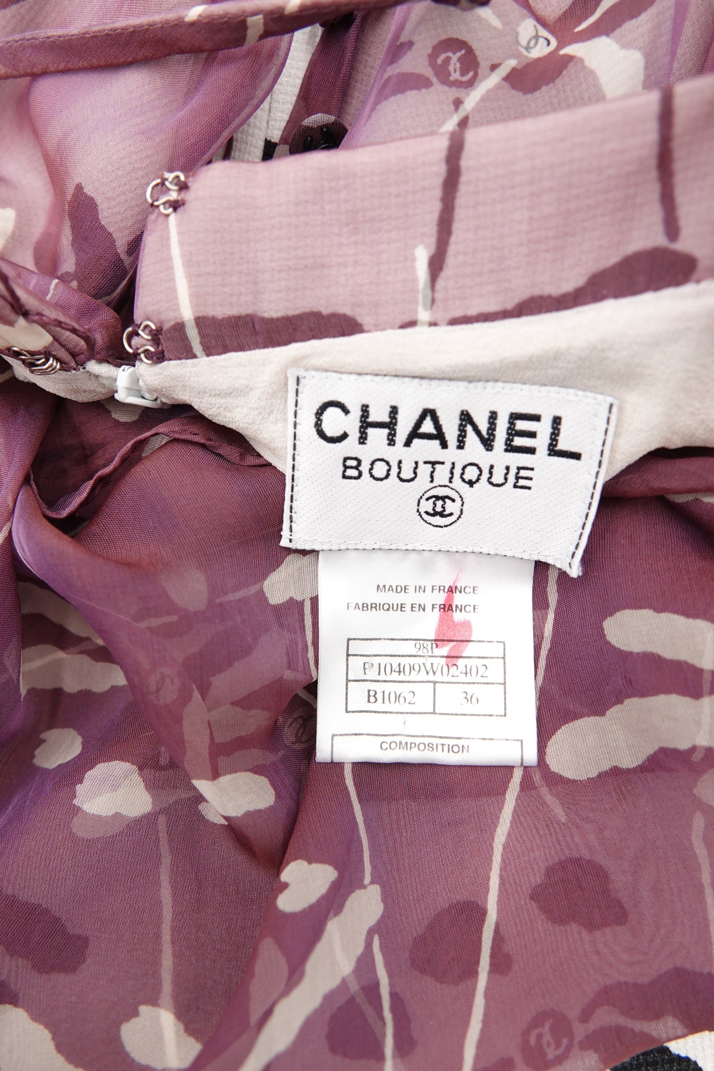 Chanel 98P authentication label close-up: white "Chanel Boutique" woven label with CC interlace logo, "Made in France" care label, on mauve dragonfly print silk chiffon, 1998