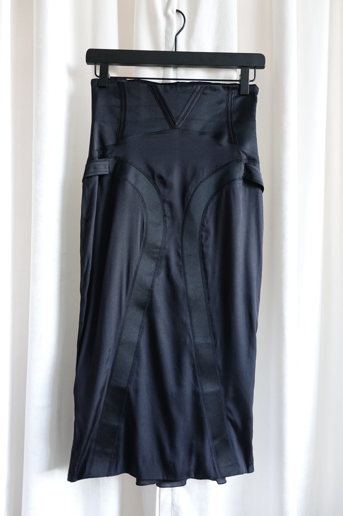 Tom Ford for Gucci FW03 black silk corset skirt on hanger: front view showing v-notch waistband, curved seam panel construction, side strap details and satin sheen, Fall 2003