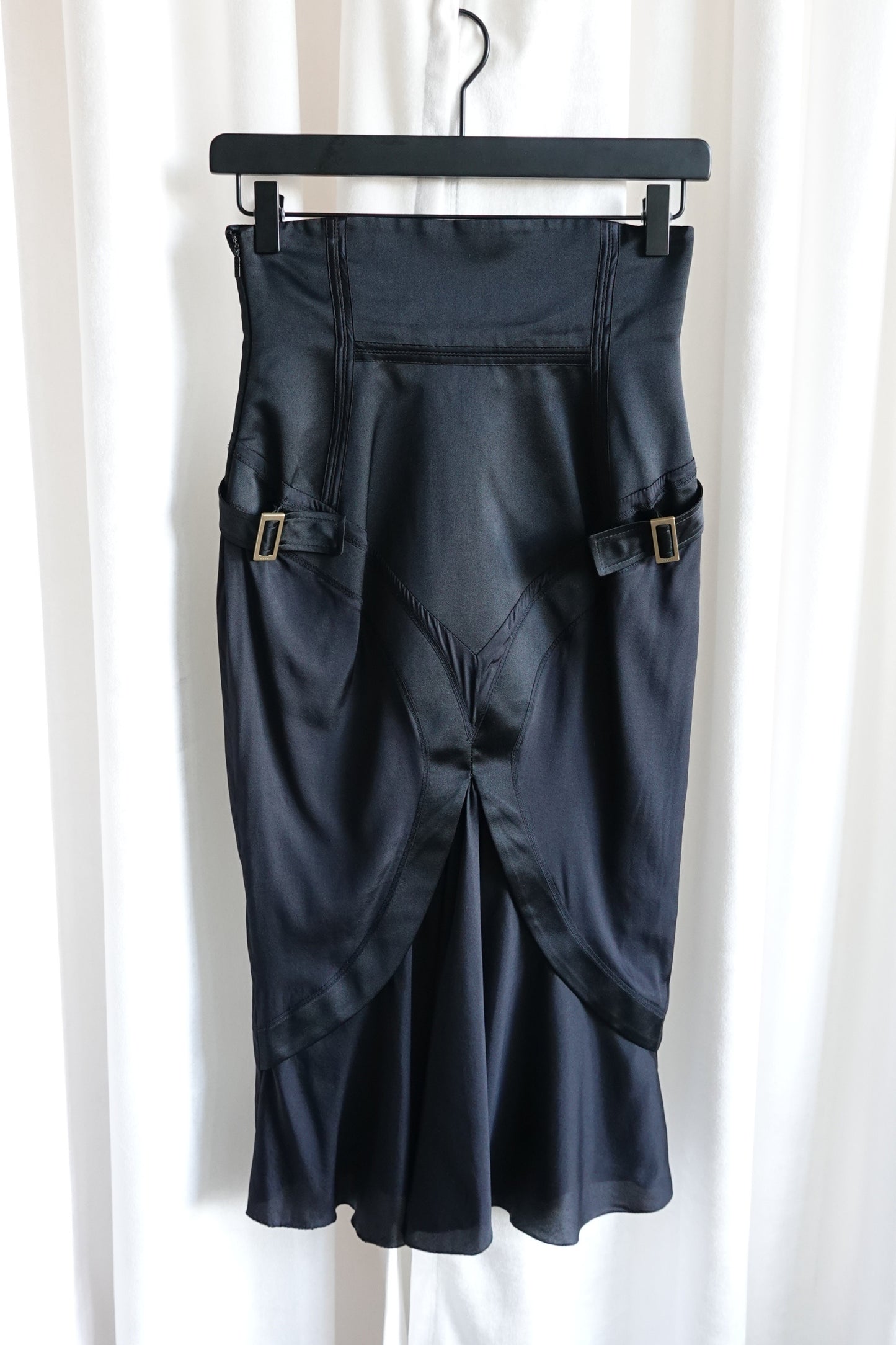 Tom Ford for Gucci FW03 black silk corset skirt on hanger: front view showing both gold-tone buckle side straps, crossover panel hem and bias-cut flared silhouette, Fall 2003