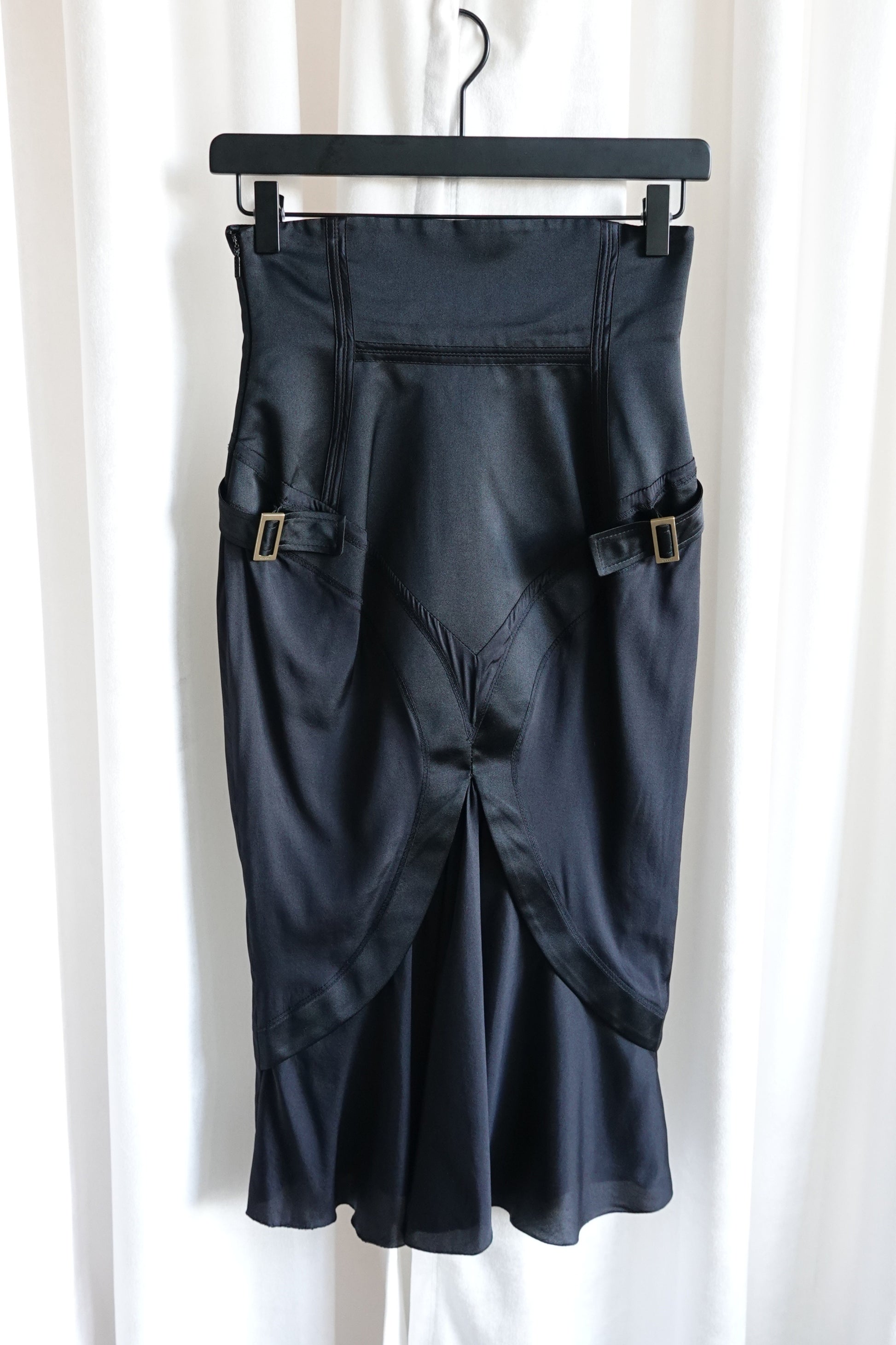 Tom Ford for Gucci FW03 black silk corset skirt on hanger: front view showing both gold-tone buckle side straps, crossover panel hem and bias-cut flared silhouette, Fall 2003