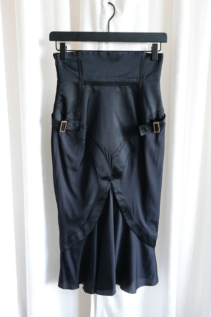Tom Ford for Gucci FW03 black silk corset skirt on hanger: front view showing both gold-tone buckle side straps, crossover panel hem and bias-cut flared silhouette, Fall 2003