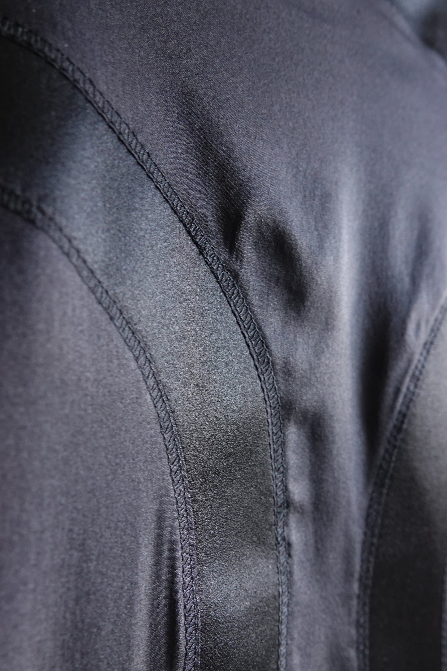 Tom Ford for Gucci FW03 black silk skirt construction detail: close-up of curved seam topstitching on bias-cut satin panel, showing tailoring quality and silk sheen, Fall 2003