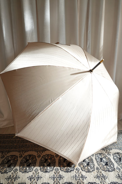 Vintage YSL Yves Saint Laurent gold umbrella: full standing view leaning against a surface showing the complete umbrella from handle to tip and overall scale