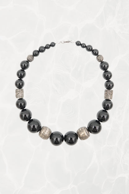 Vintage 1980s black onyx graduated beaded necklace with engraved silver spacers — full length on background