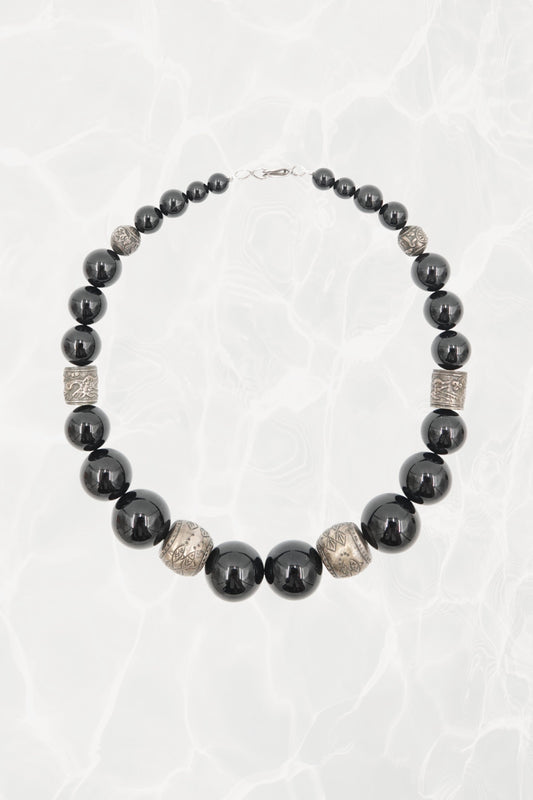Vintage 1980s black onyx graduated beaded necklace with engraved silver spacers — full length on background
